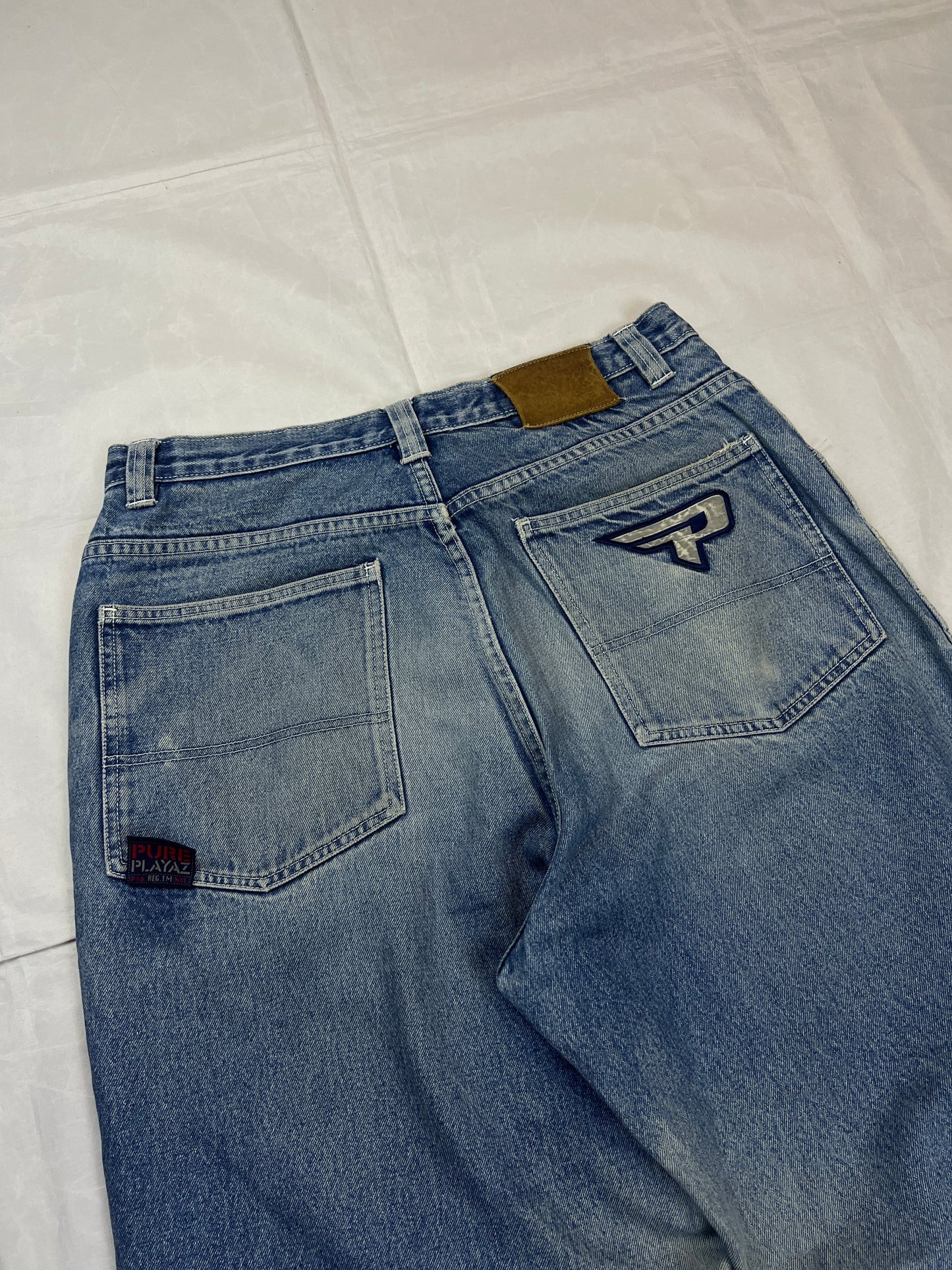 Pure Playaz blue denim jeans with distressed rips, faded wash, and branded patches.