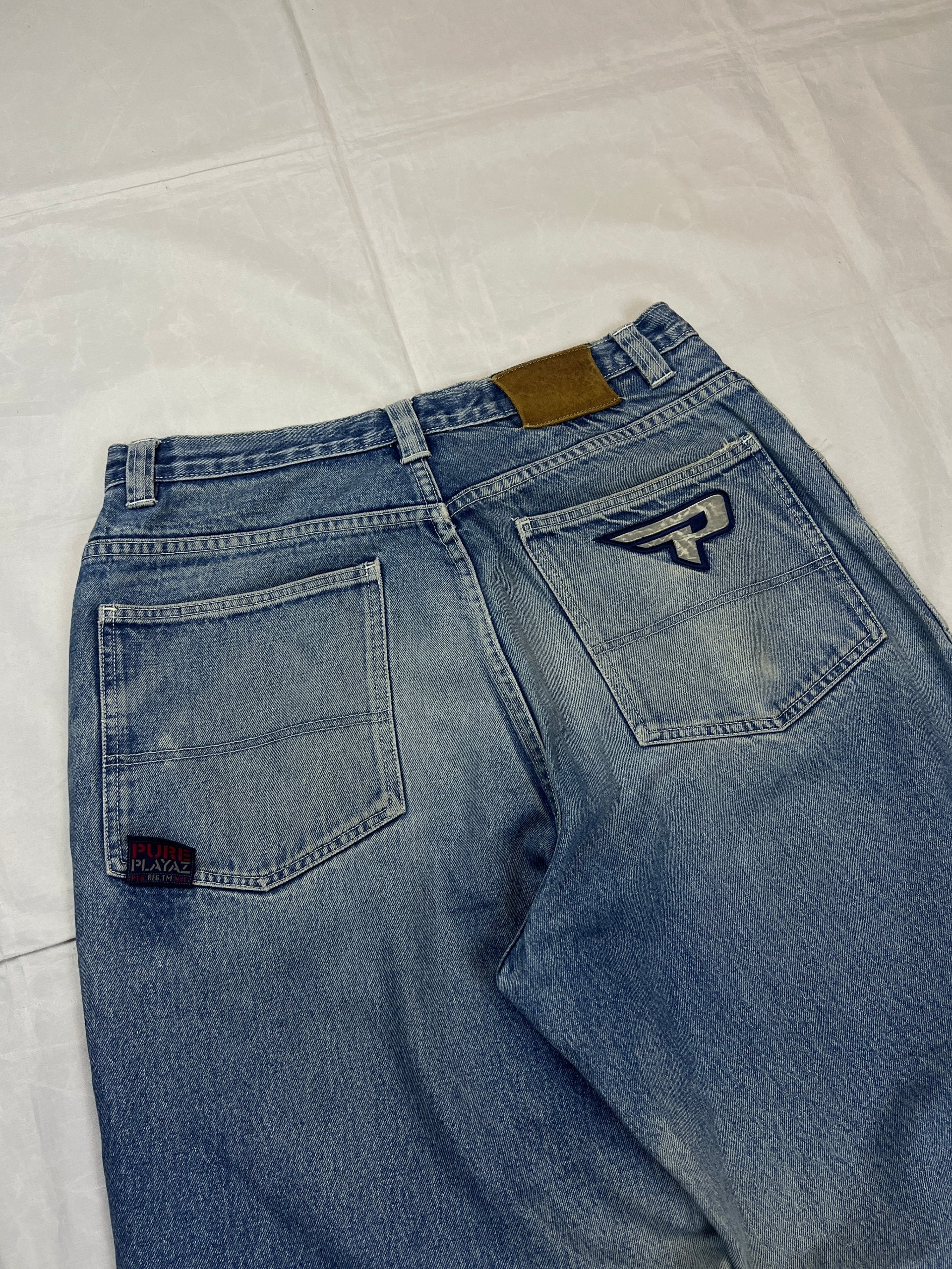 Pure Playaz blue denim jeans with distressed rips, faded wash, and branded patches.