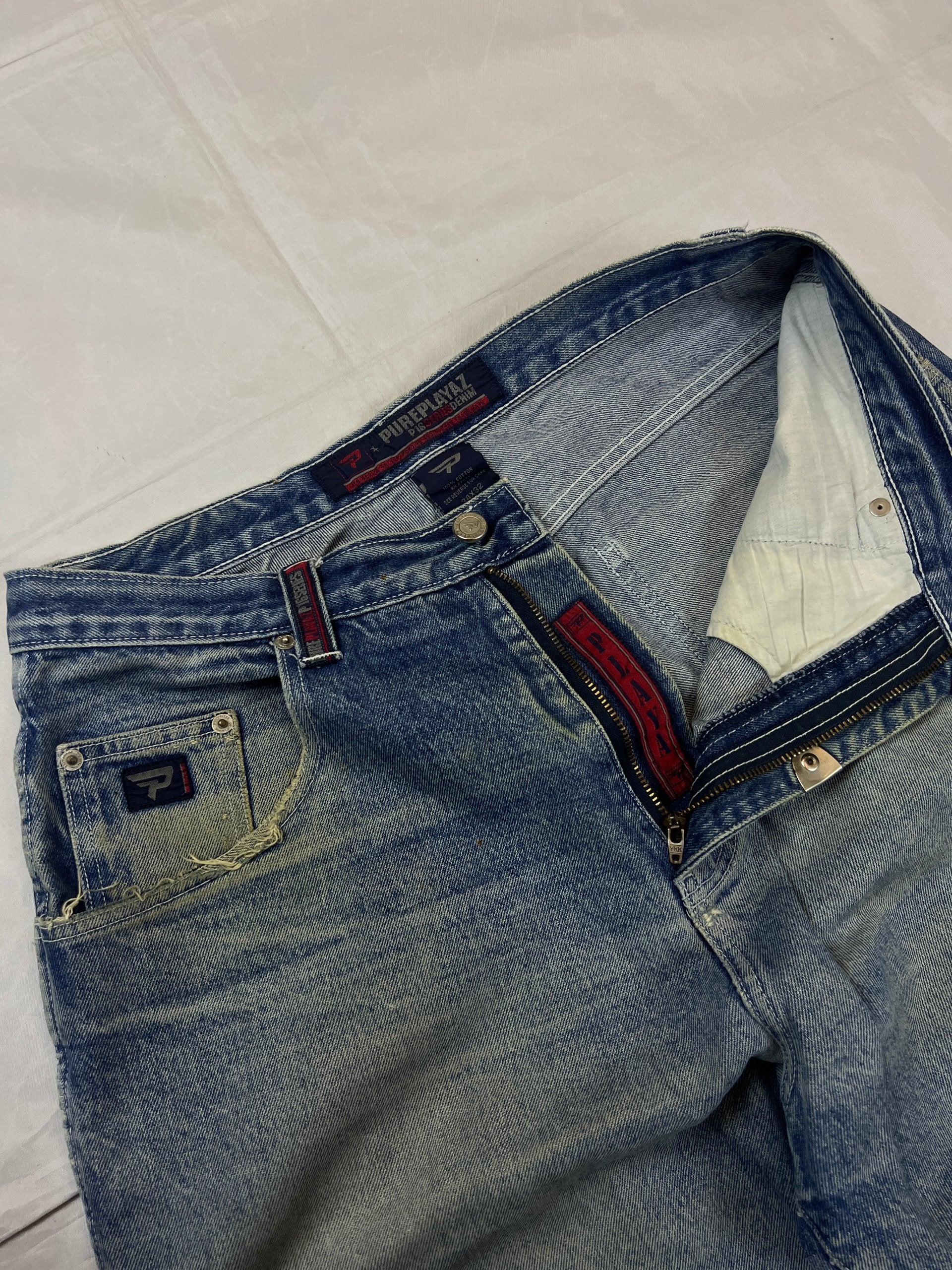 Pure Playaz blue denim jeans with distressed rips, faded wash, and branded patches.