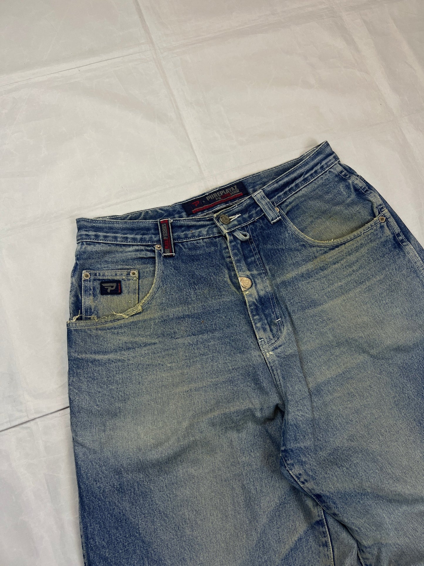 Pure Playaz blue denim jeans with distressed rips, faded wash, and branded patches.