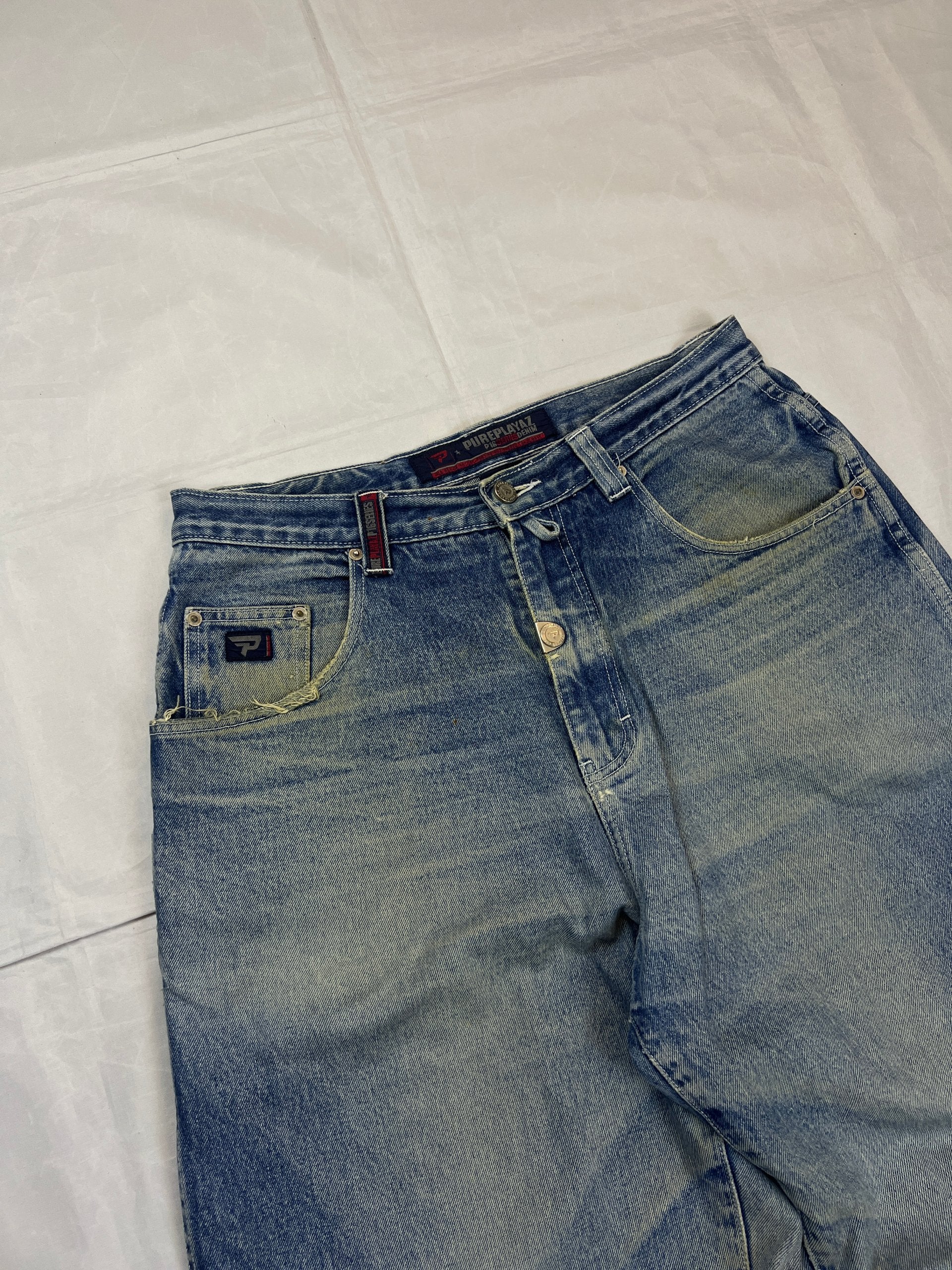 Pure Playaz blue denim jeans with distressed rips, faded wash, and branded patches.