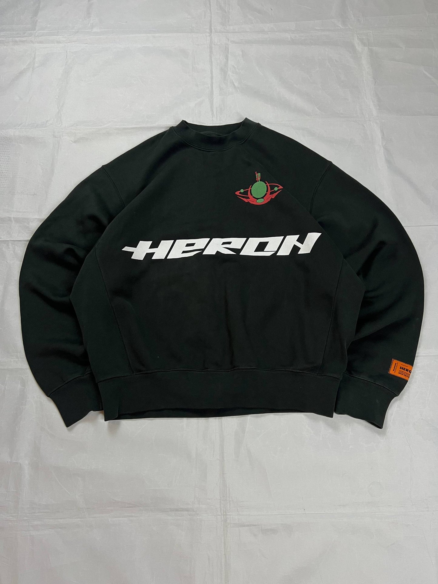 Heron Preston black graphic crewneck sweatshirt with white 'HERON' text and orange label patch.
