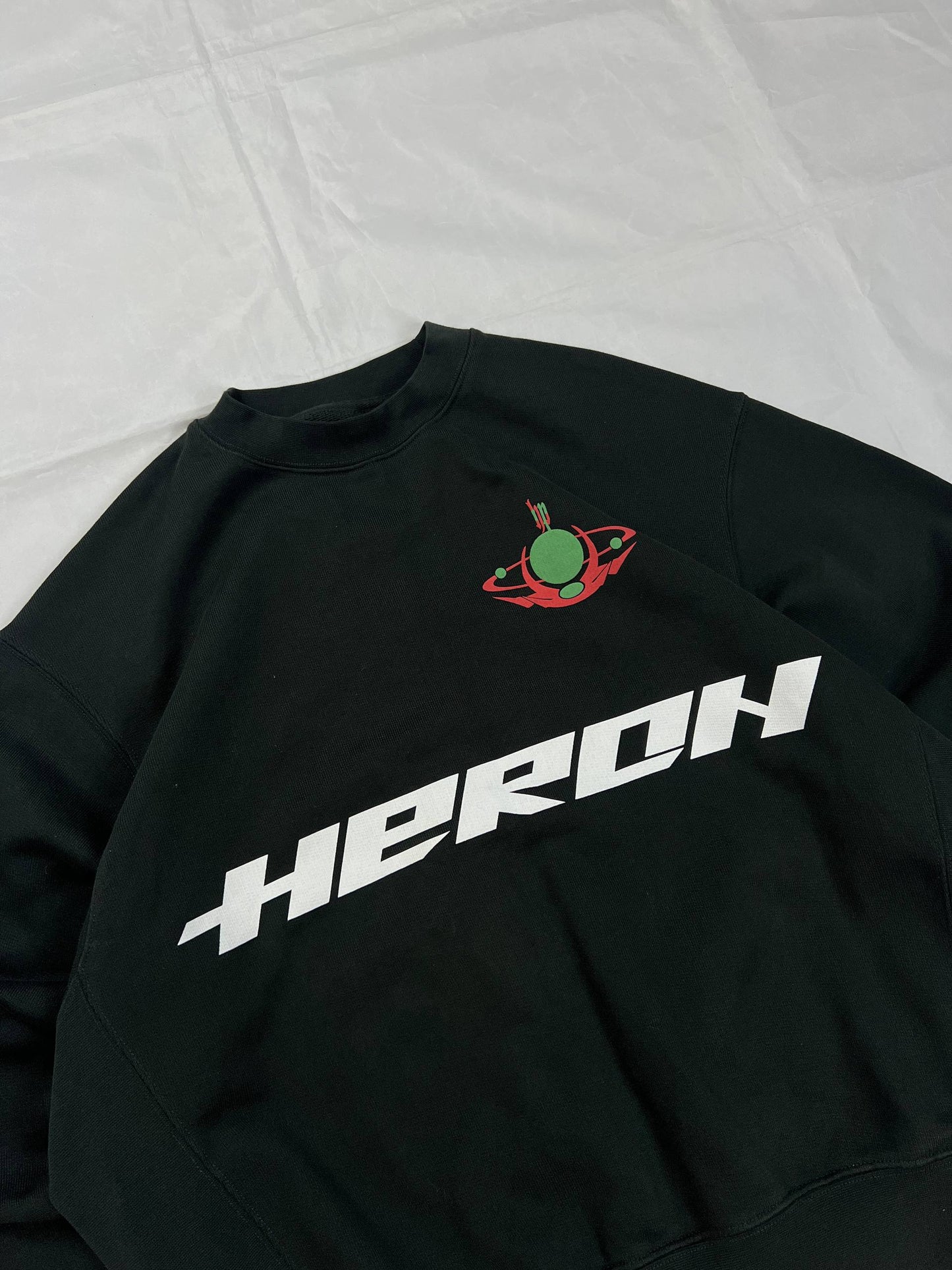 Heron Preston black graphic crewneck sweatshirt with white 'HERON' text and orange label patch.