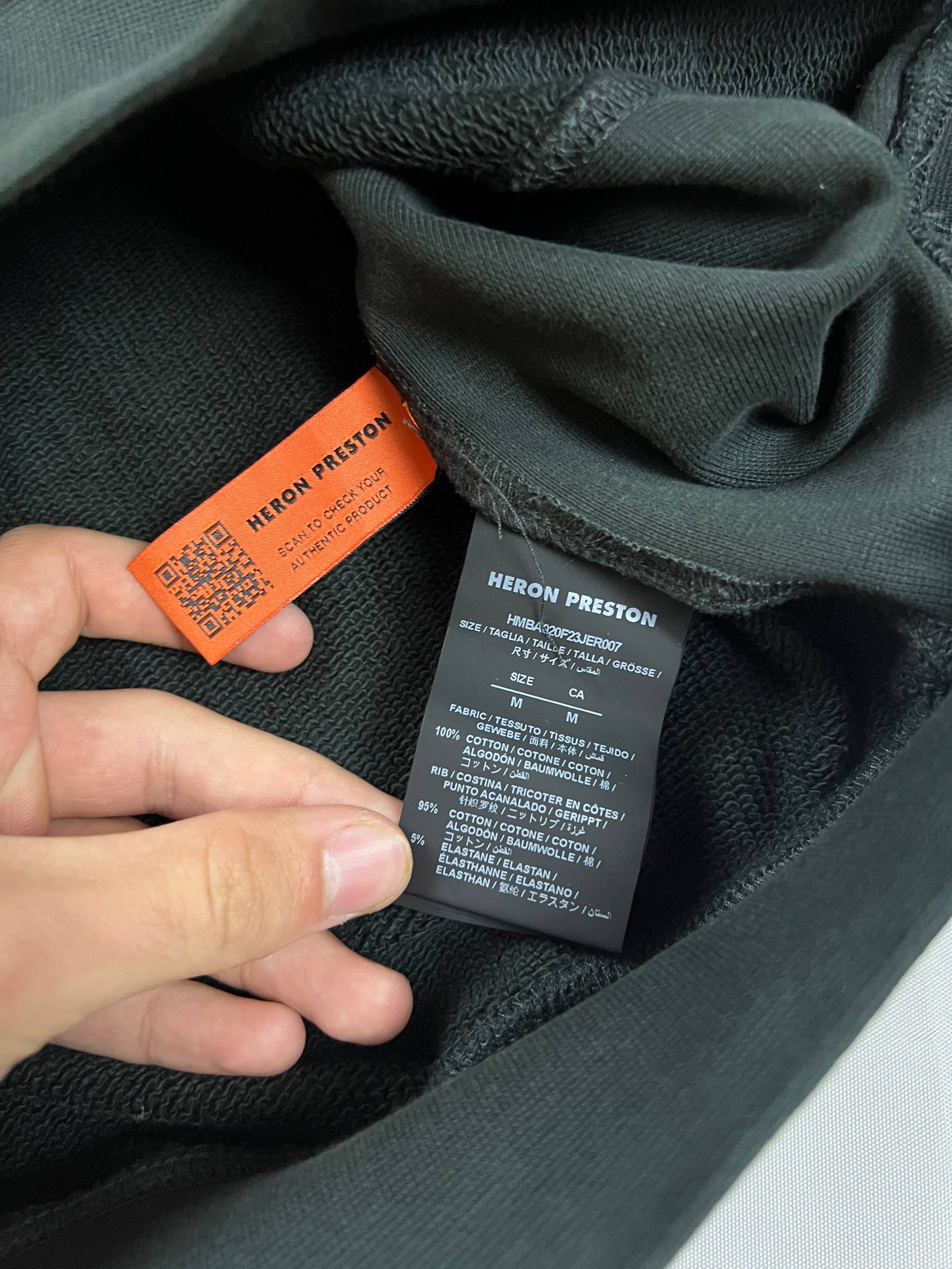 Heron Preston black graphic crewneck sweatshirt with white 'HERON' text and orange label patch.