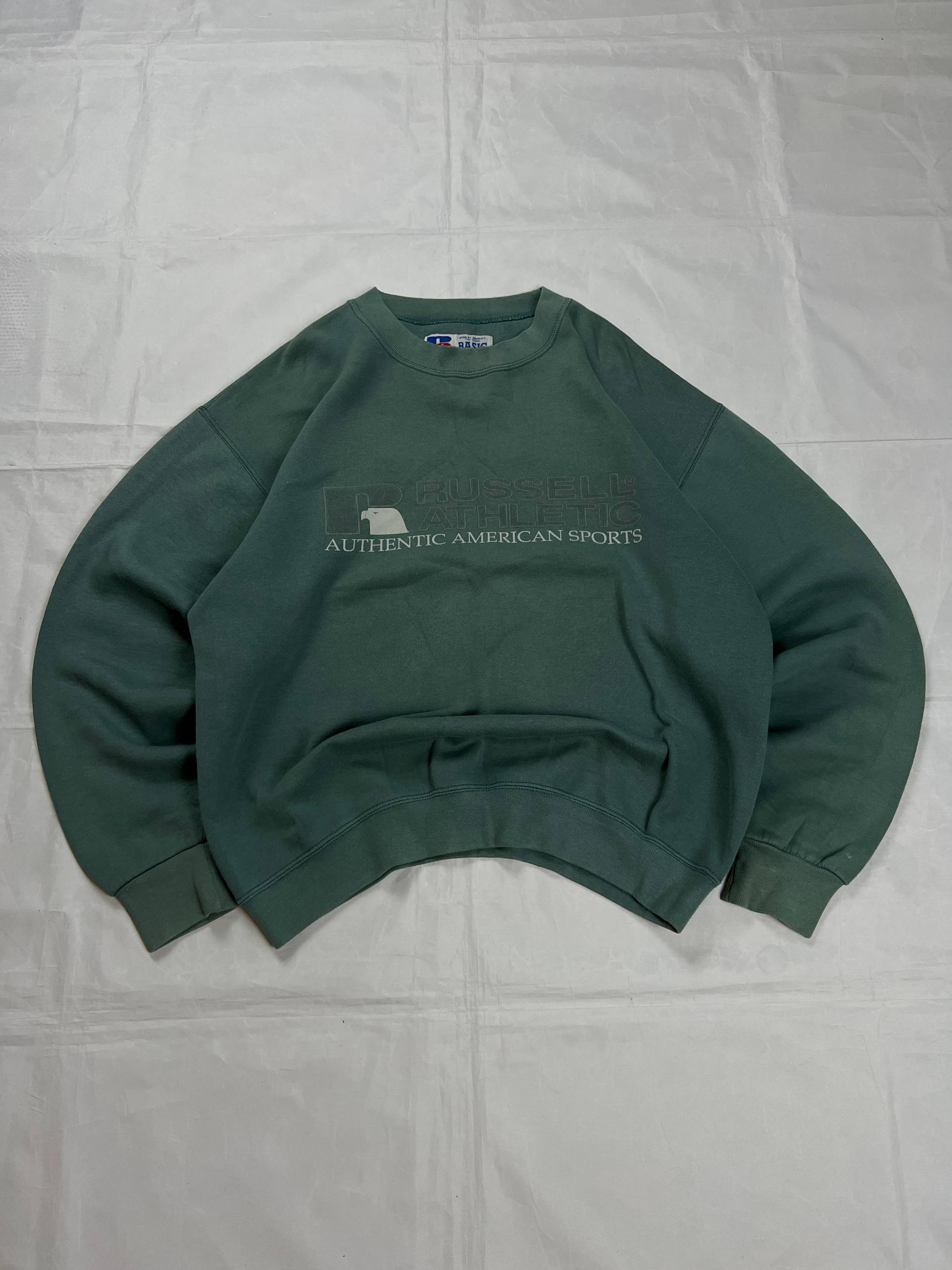 Russell Athletic green crewneck sweatshirt with subtle AUTHENTIC AMERICAN SPORTS branding and ribbed cuffs.