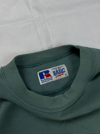 Russell Athletic green crewneck sweatshirt with subtle AUTHENTIC AMERICAN SPORTS branding and ribbed cuffs.
