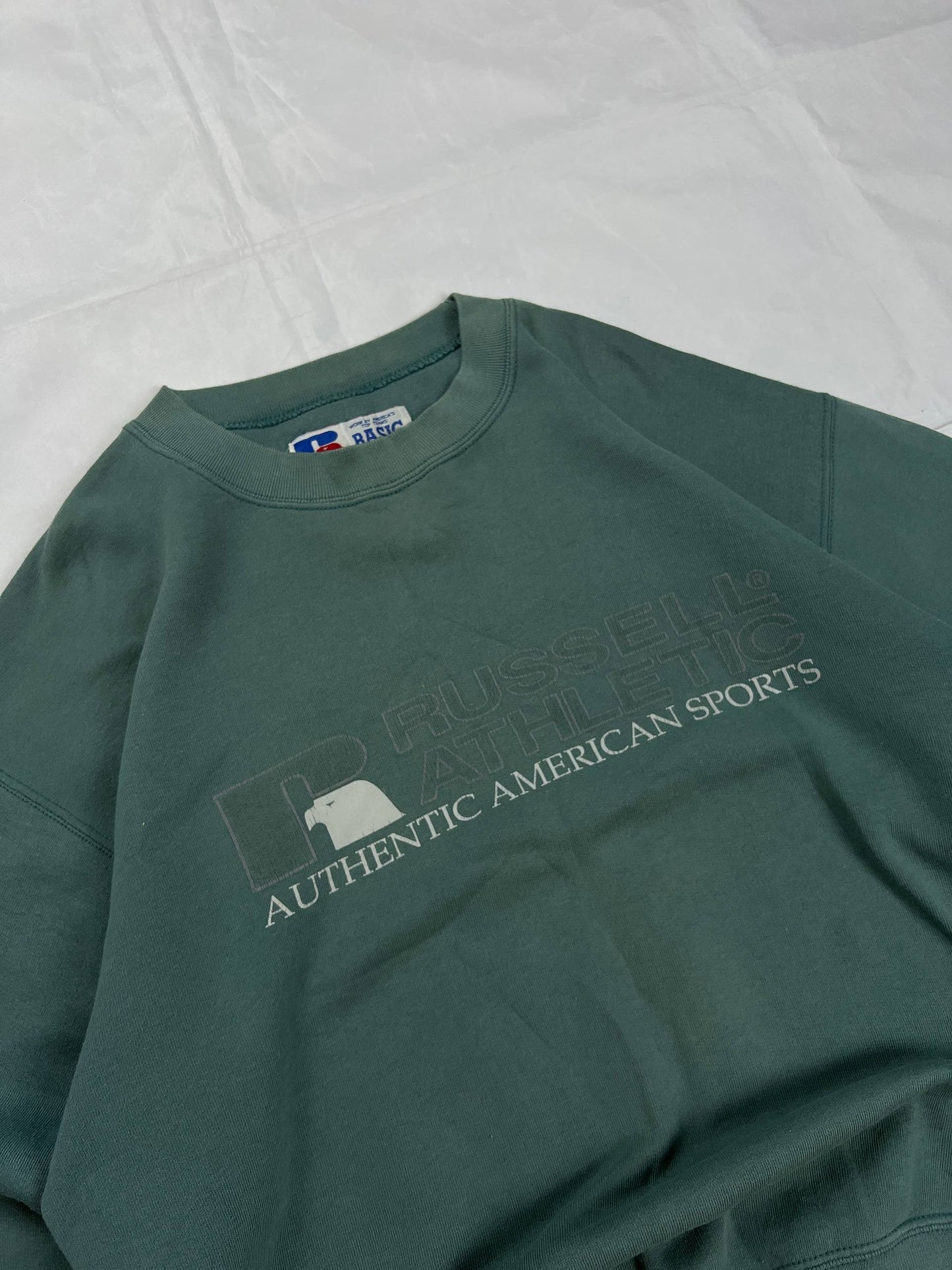 Russell Athletic green crewneck sweatshirt with subtle AUTHENTIC AMERICAN SPORTS branding and ribbed cuffs.