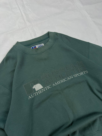 Russell Athletic green crewneck sweatshirt with subtle AUTHENTIC AMERICAN SPORTS branding and ribbed cuffs.