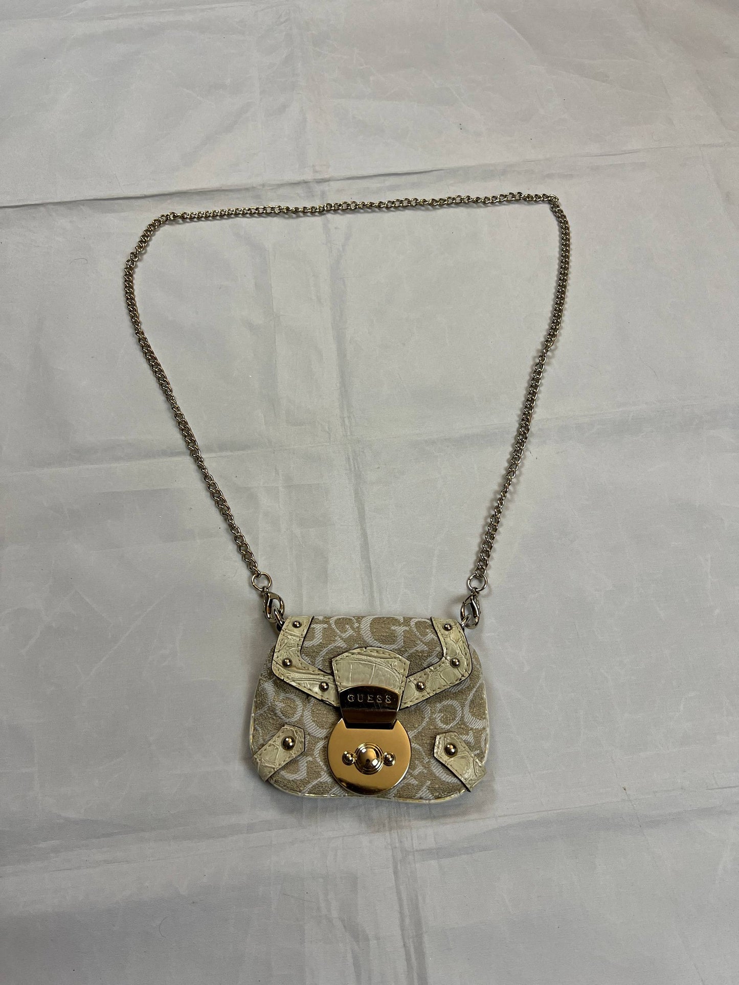 Guess beige mini crossbody bag with white signature print and gold-tone chain strap.