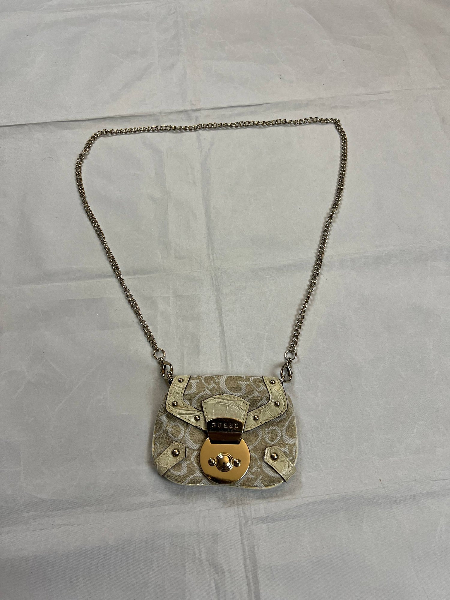 Guess beige mini crossbody bag with white signature print and gold-tone chain strap.