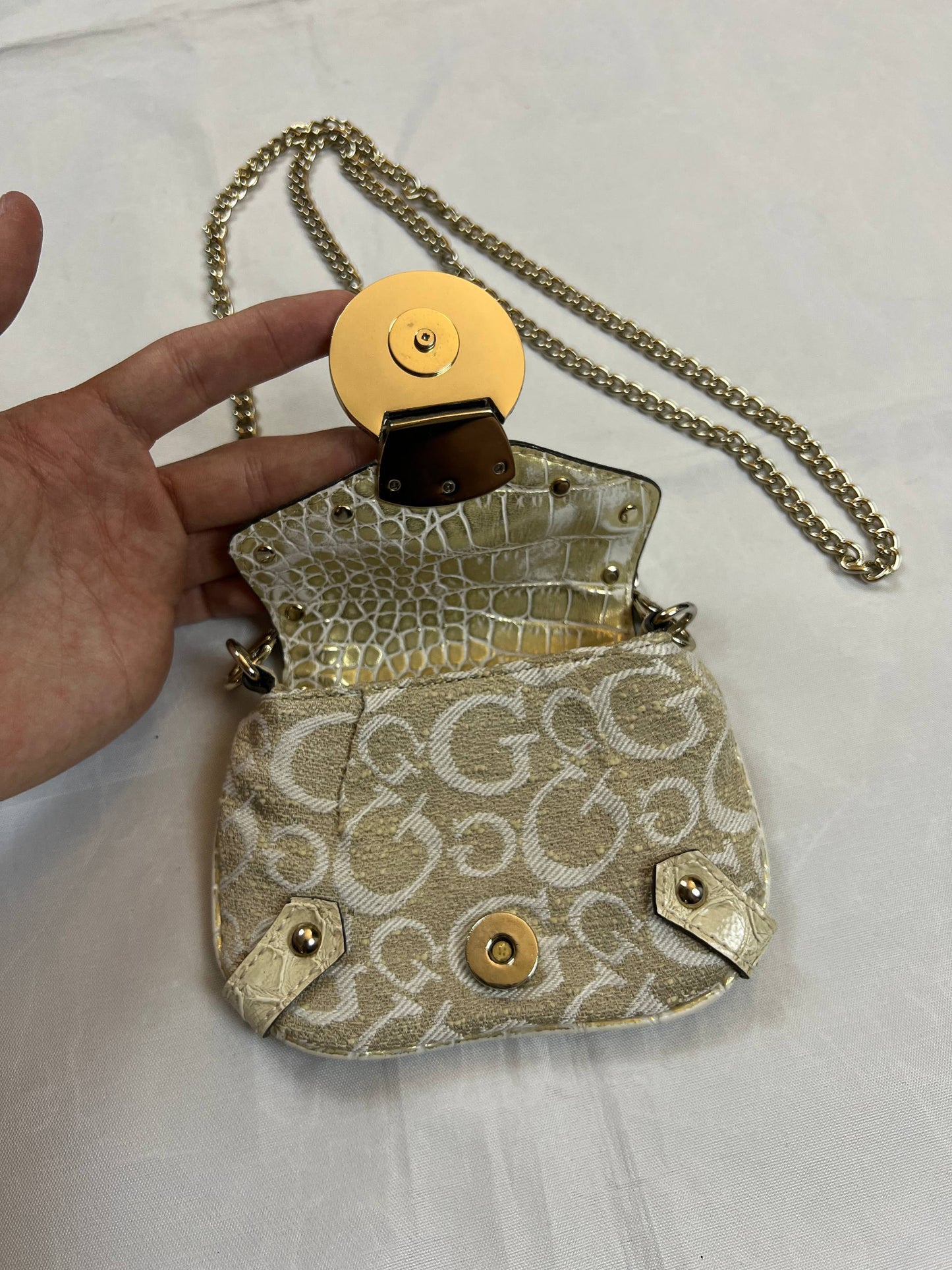Guess beige mini crossbody bag with white signature print and gold-tone chain strap.