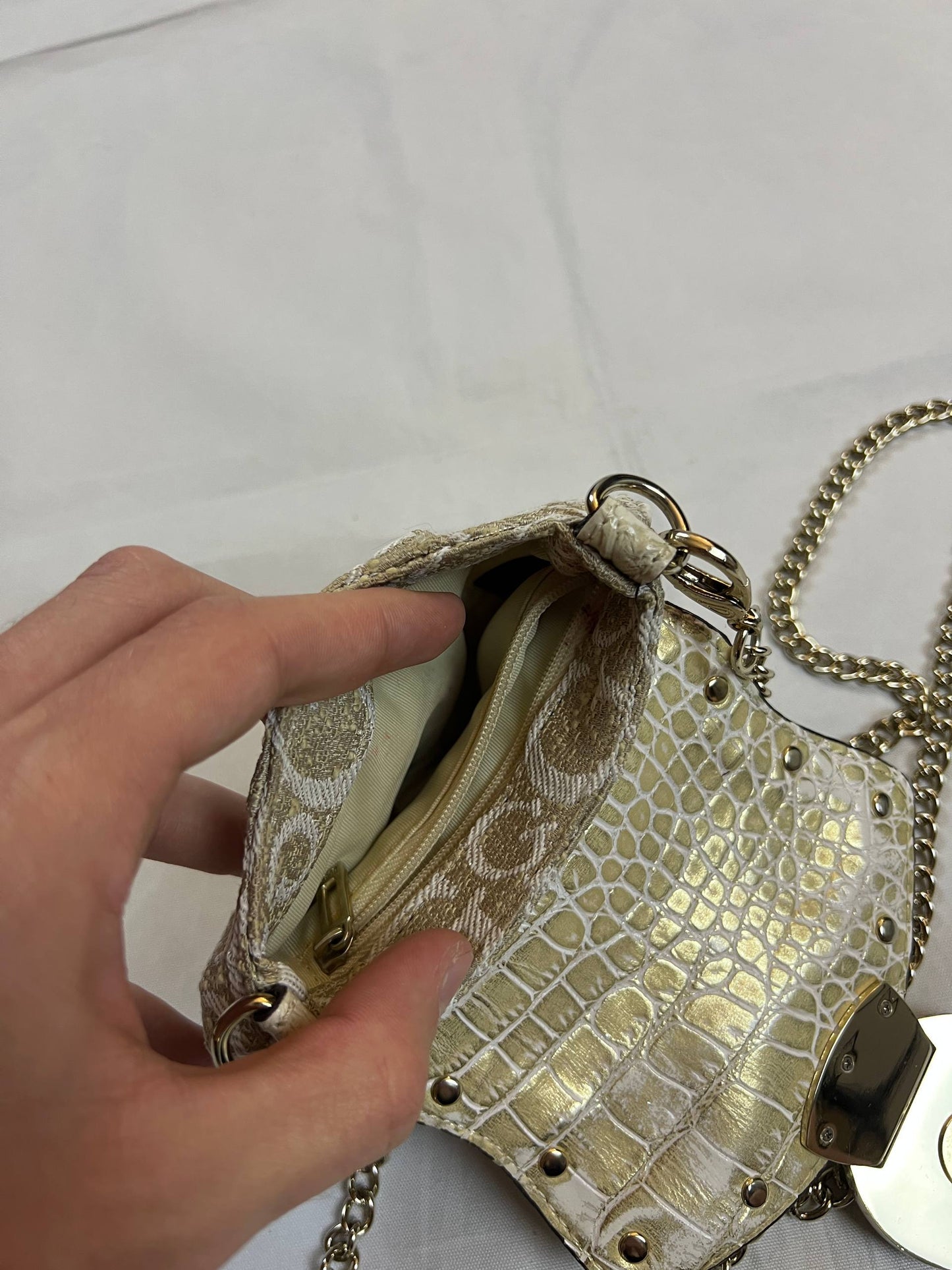 Guess beige mini crossbody bag with white signature print and gold-tone chain strap.