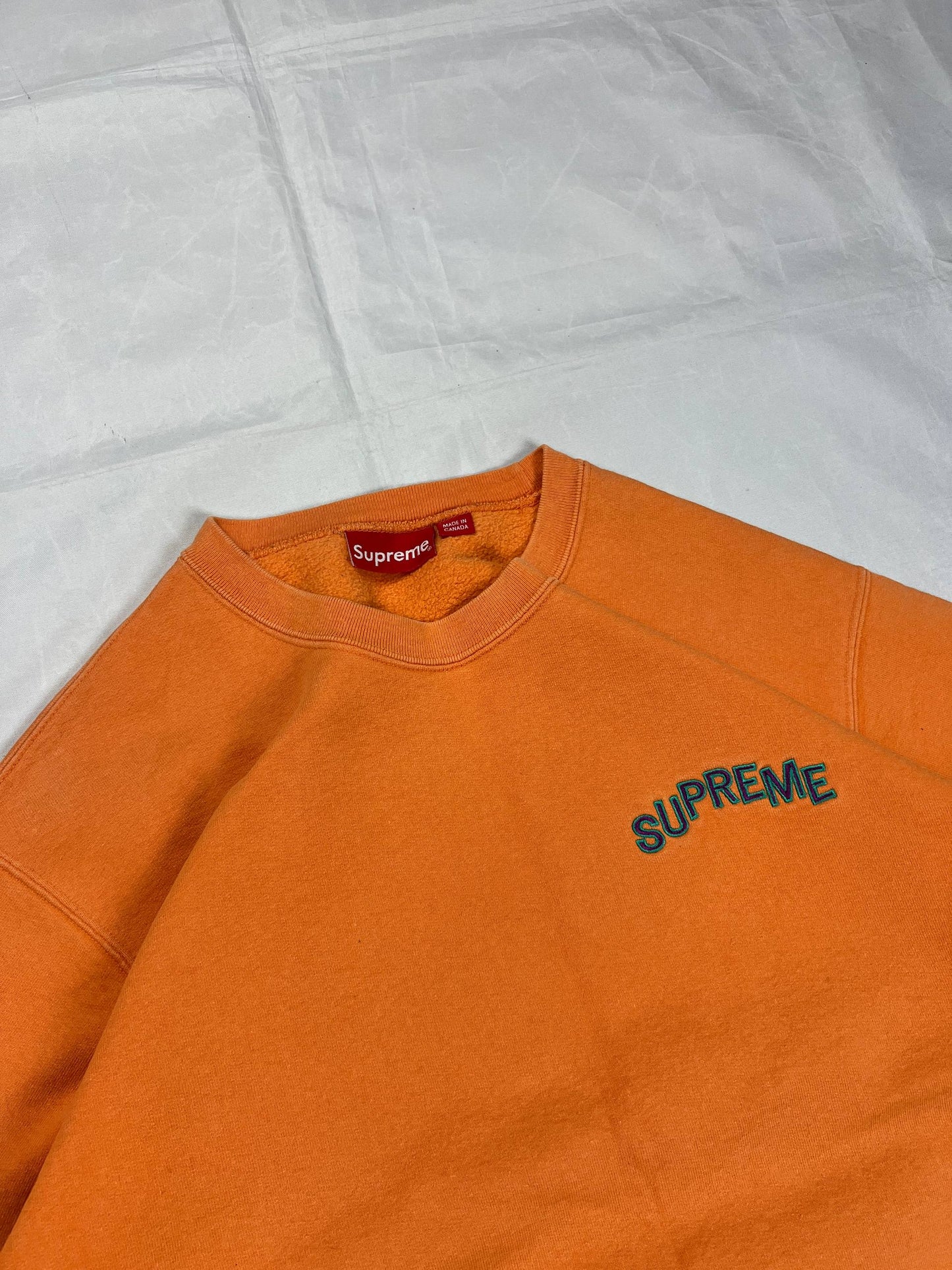 Supreme orange crewneck sweatshirt large embroidered logo on chest, soft cotton material.