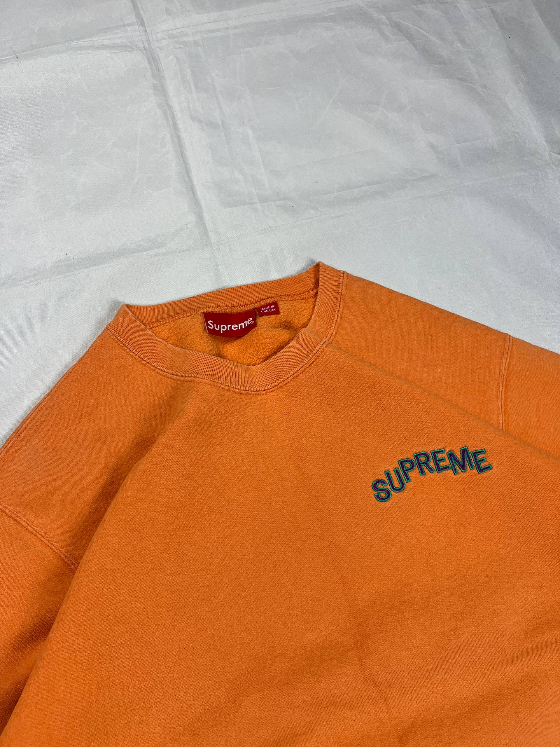 Supreme orange crewneck sweatshirt large embroidered logo on chest, soft cotton material.