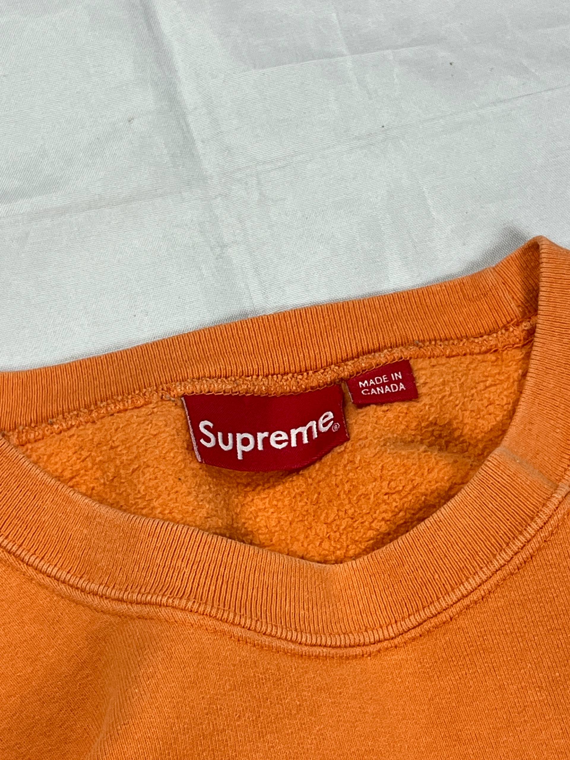 Supreme orange crewneck sweatshirt large embroidered logo on chest, soft cotton material.